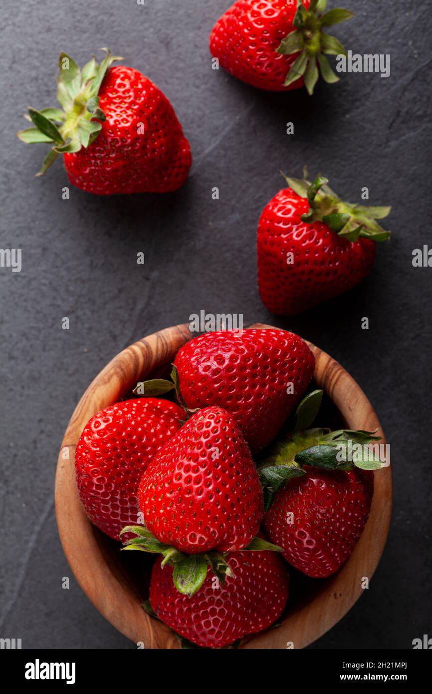 Una ciotola di fragole in legno su un tavolo con sfondo scuro. Immagine modica a bassa luce con snack sani, concetti di frutta fresca. Vista dall'alto Flat Lay Foto Stock