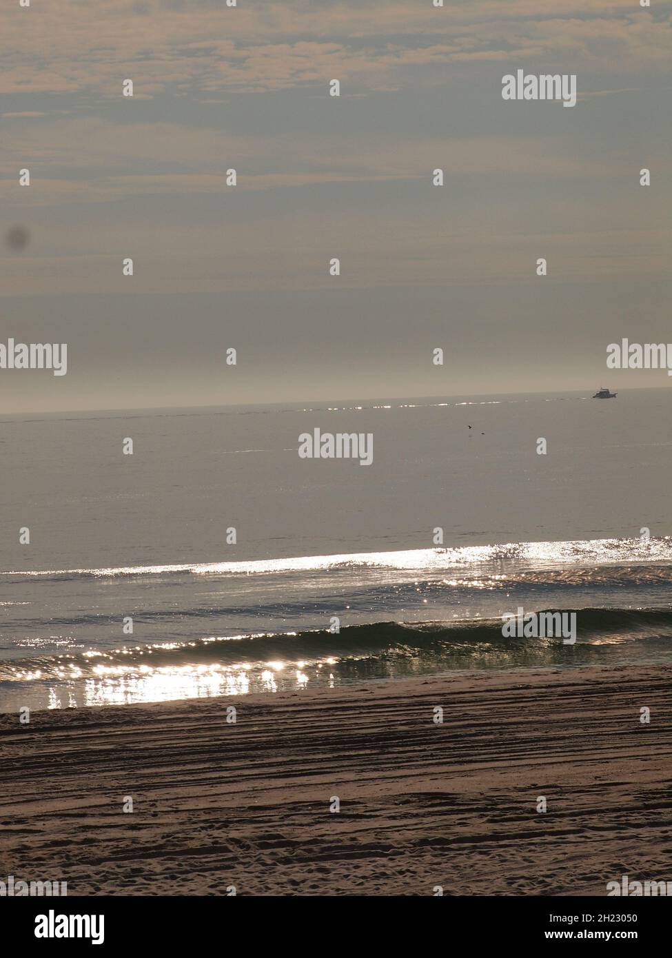 Onde scintillanti che si infrangono lungo la costa del New Jersey in Ocean Beach. In lontananza è una barca da pesca solare che esce. Foto Stock