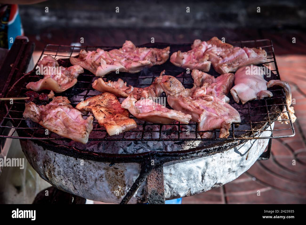 Molte orecchie di maiale grigliate su una griglia di acciaio su una stufa a carbone. (Cibo di stile thailandese), fuoco selettivo. Foto Stock