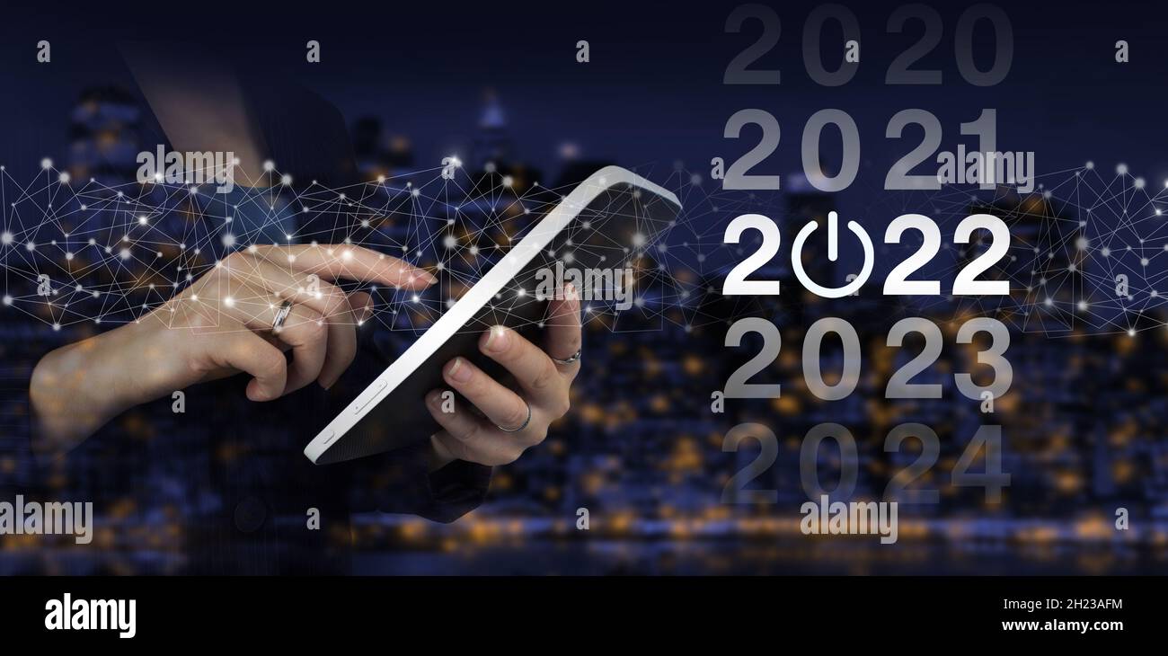 Concetto di nuovo anno. Mano toccare tablet bianco con ologramma digitale 2022 segno sulla città scuro sfondo sfocato. anno nuovo 2022. Concept inizio nuovo anno 2022 Foto Stock