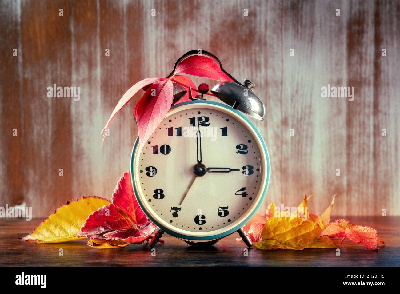 Concetto di ora legale, ritorno in autunno. Una sveglia d'epoca con foglie d'autunno su un rustico sfondo di legno Foto Stock