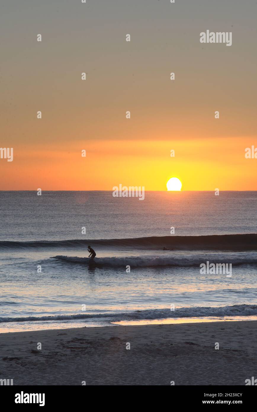 Il surfista corre un'onda mentre il sole sorge Foto Stock