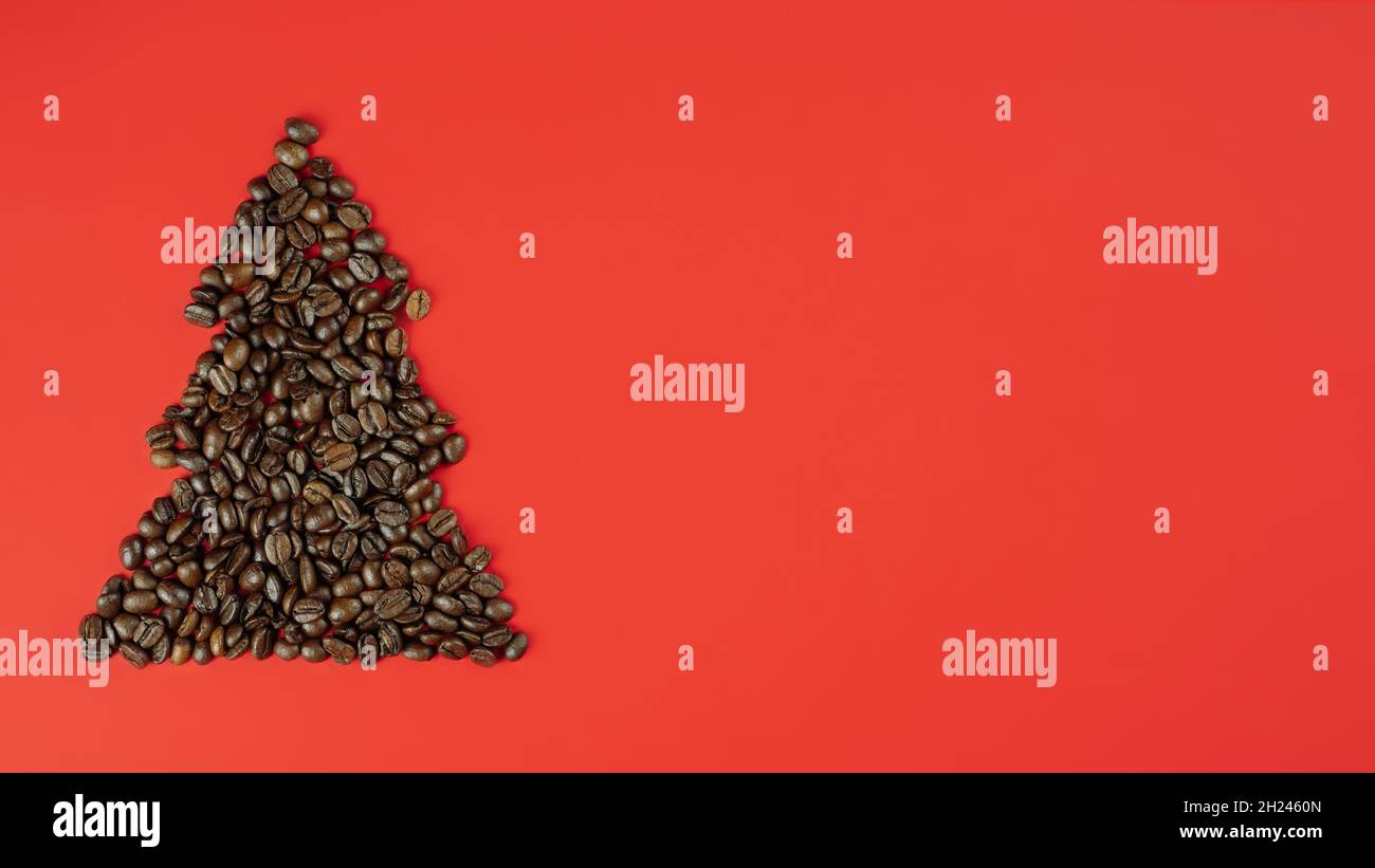 Chicchi di caffè marroni disposti a forma di albero di Natale su sfondo rosso. Banner. Disposizione piatta. Spazio di copia Foto Stock