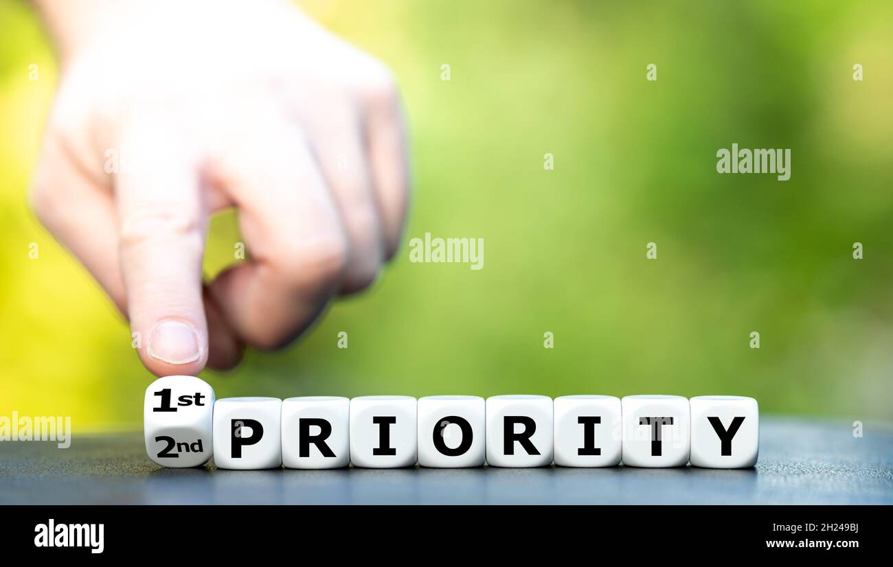 La mano gira i dadi e cambia l'espressione '2a priorità' in '1a priotity'. Foto Stock