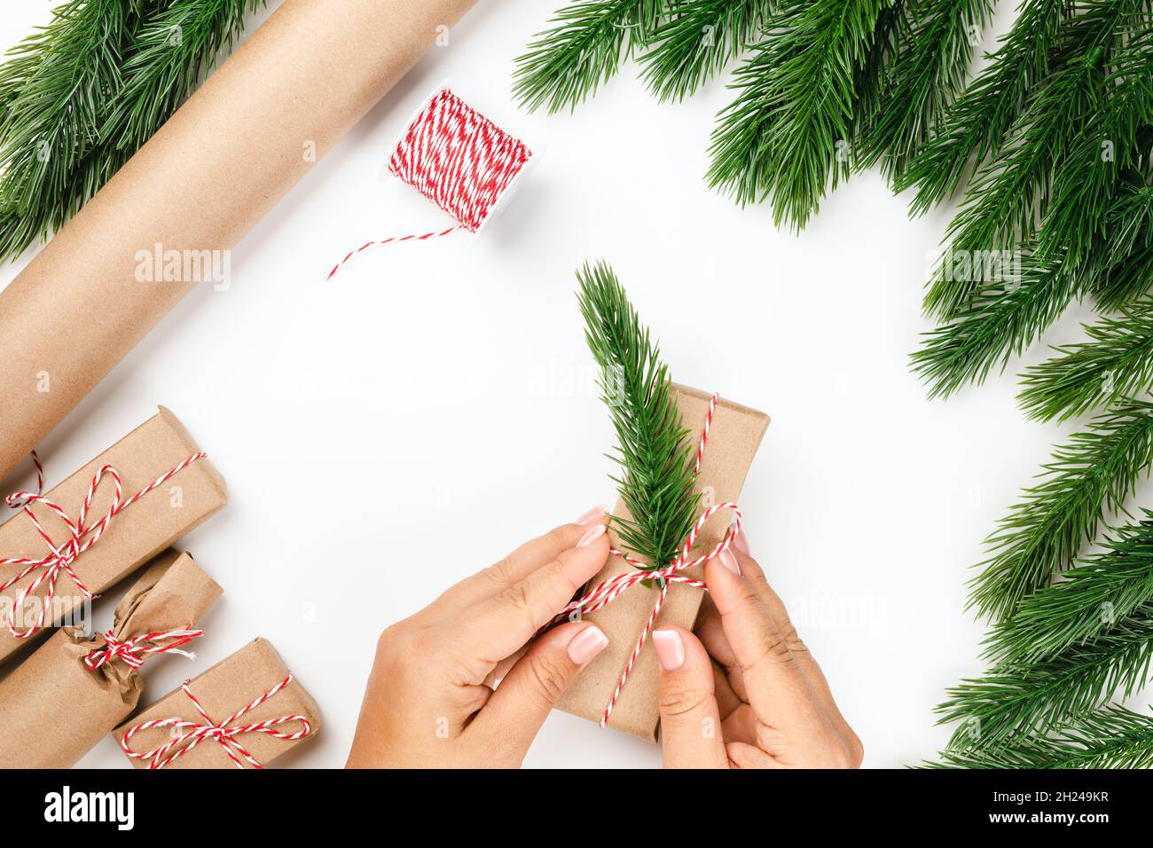 Vista dall'alto processo di imballaggio e decorazione regali di Natale in cornice di rami di albero di Natale, carta artigianale Foto Stock