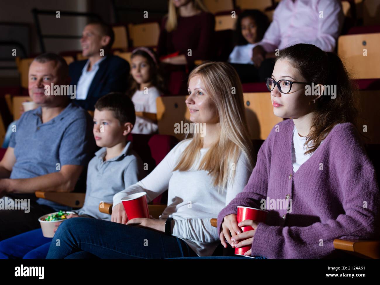 Famiglia cordiale di quattro persone seduto con popcorn e bevande al cinema, guardando film con interesse. Divertimento e divertimento per tutta la famiglia Foto Stock