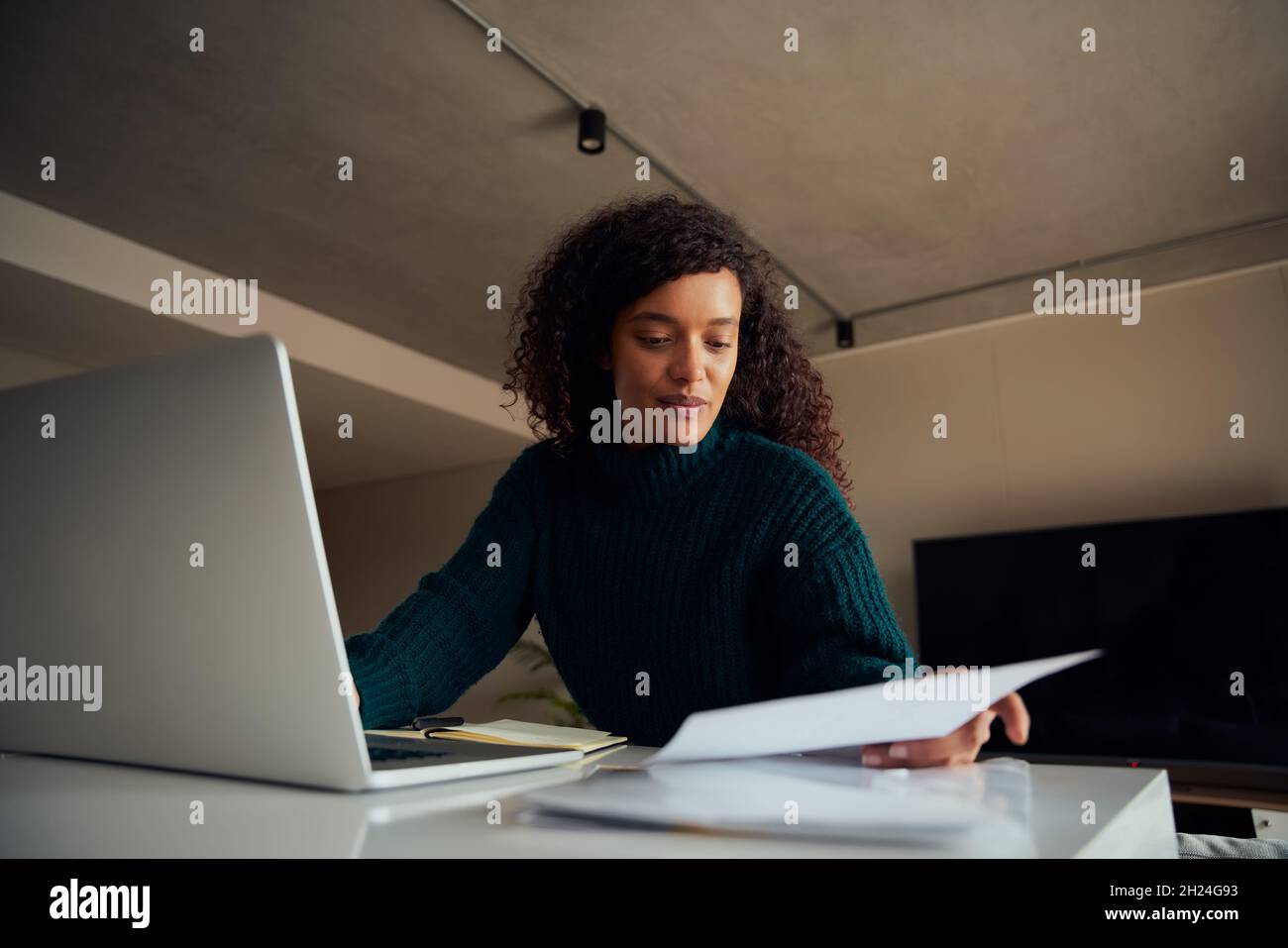 Donna afroamericana adulta riferendosi alle note mentre lavora sul laptop seduto al bancone della cucina Foto Stock