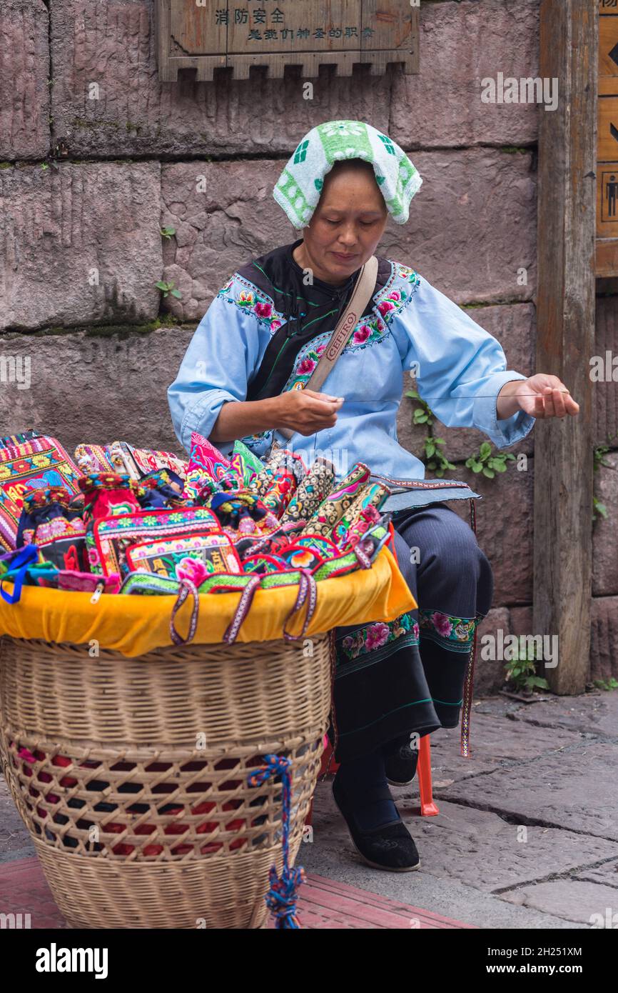 Una donna di Miao etnico sews borse souvenir sulla strada nella città antica di Fenghuang, Cina. Foto Stock