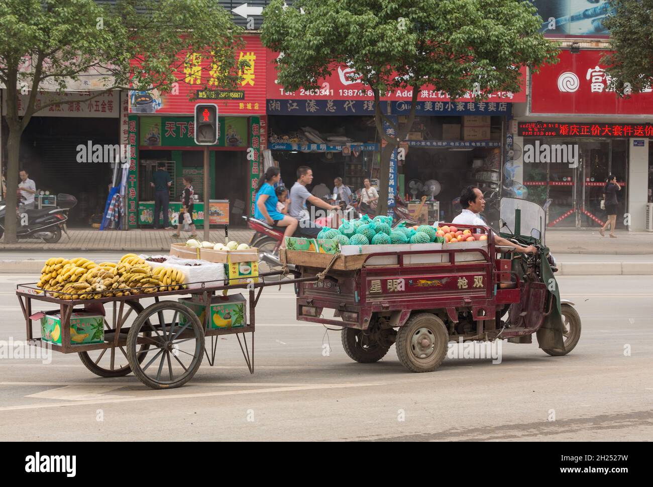 Un carrello motorizzato a tre ruote traina un carrello da frutta, portando i prodotti sul mercato in Cina. Foto Stock