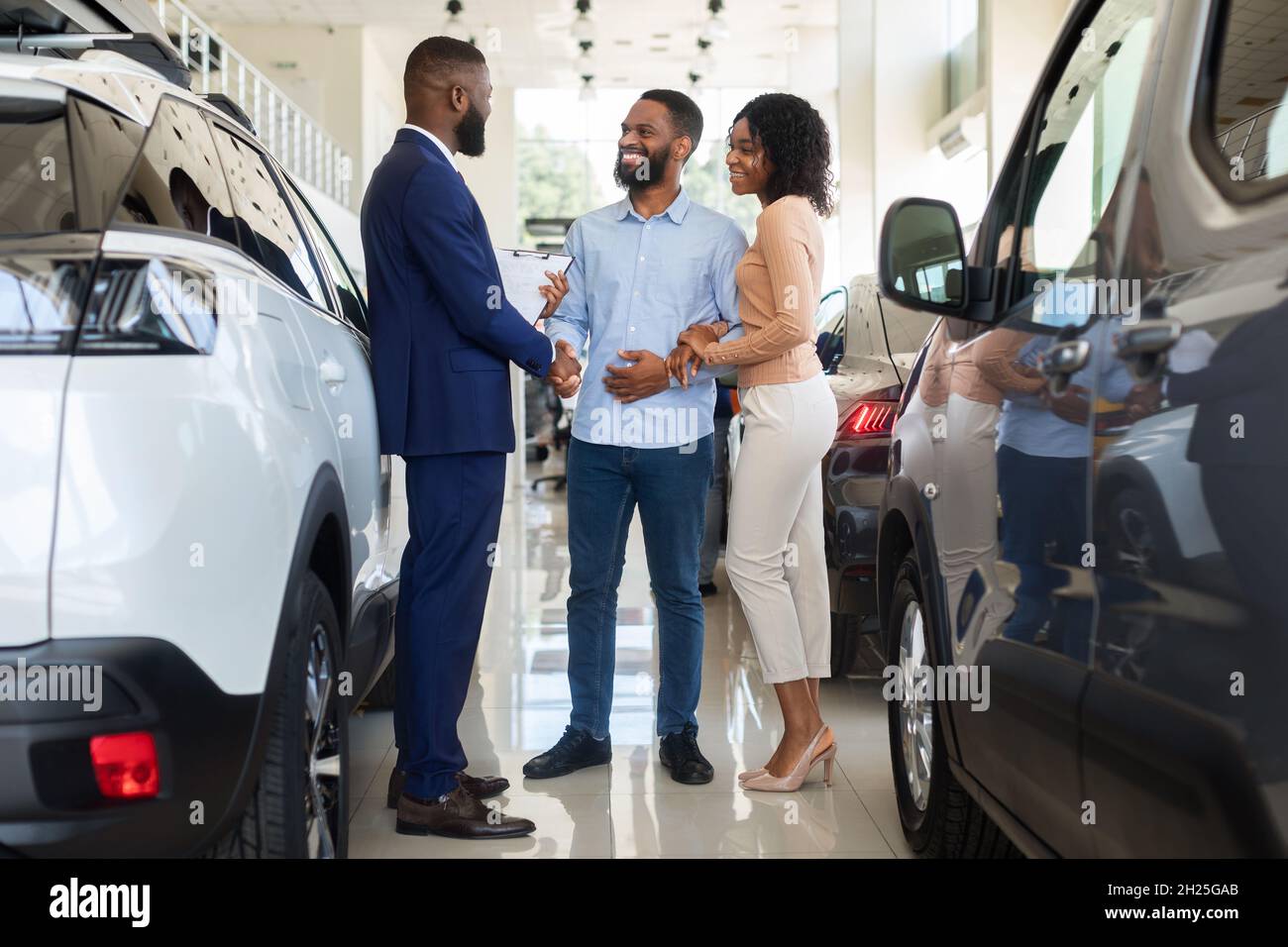 Acquisto auto. I clienti felici abbellono Handshaking con Manager in Auto Salon Foto Stock