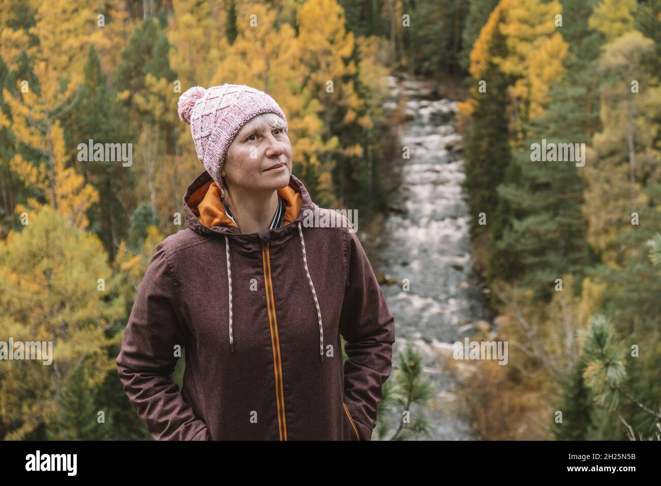 Un ritratto autentico di una donna adulta viaggiatore in abiti caldi sulla cima della montagna, sullo sfondo di un autunno foresta.Looks up.Eco turismo. Foto Stock