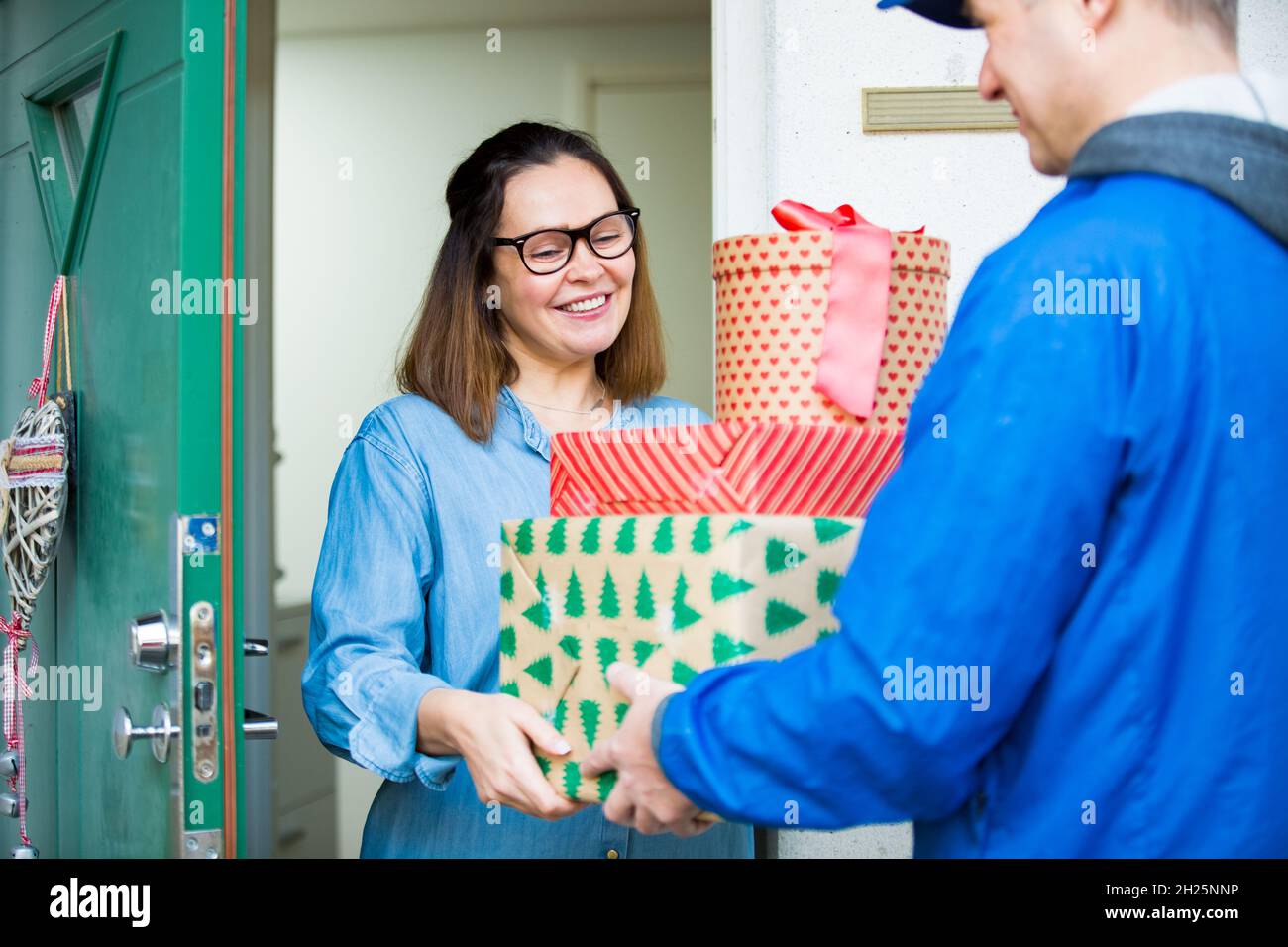 Addetto alla consegna che porta pacchetti vacanza. Donna a casa in piedi in porta, ricevendo pacchi per regali di Natale. Foto Stock