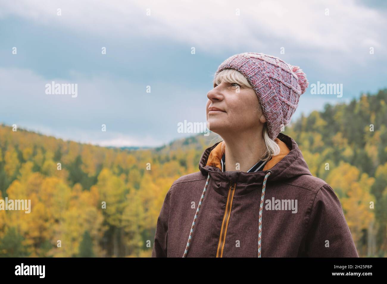 Un autentico ritratto di viaggiatore adulto di mezza età in abiti caldi in cima alla montagna, sullo sfondo del cielo e della foresta in autunno. Foto Stock
