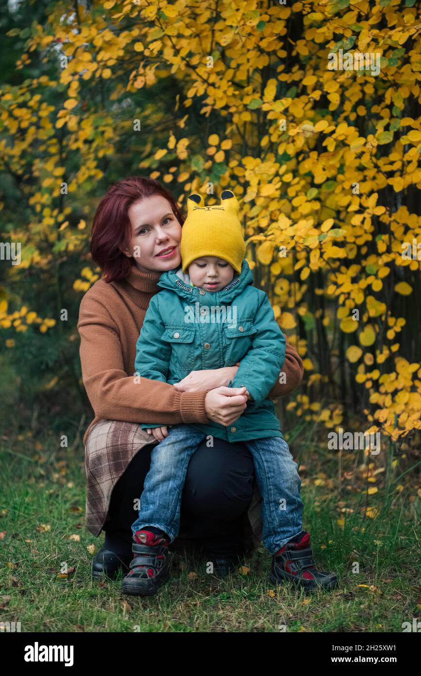 Piccolo ragazzo caucasico e sua madre contro la foresta gialla autunno. Foto Stock