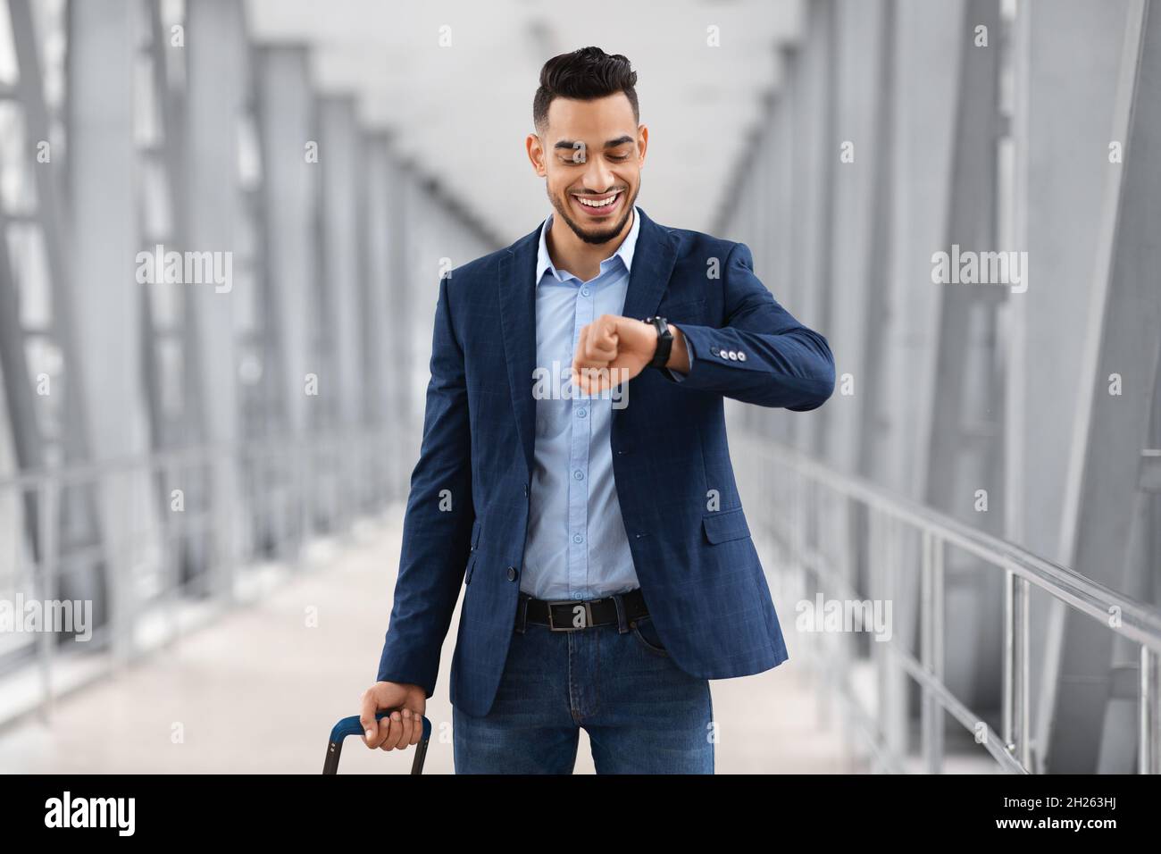 Giovane uomo d'affari arabo a piedi con Suitcase in aeroporto e guardando il orologio da polso Foto Stock