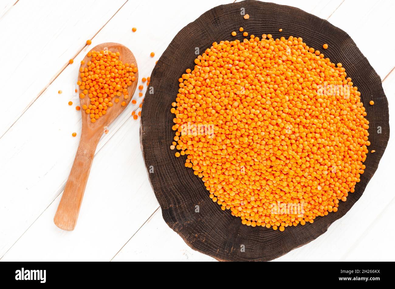 Lenticchie rosse e bulgur su un piatto di legno scuro e un cucchiaio di legno in piedi su un tavolo di legno bianco con spazio copia Foto Stock