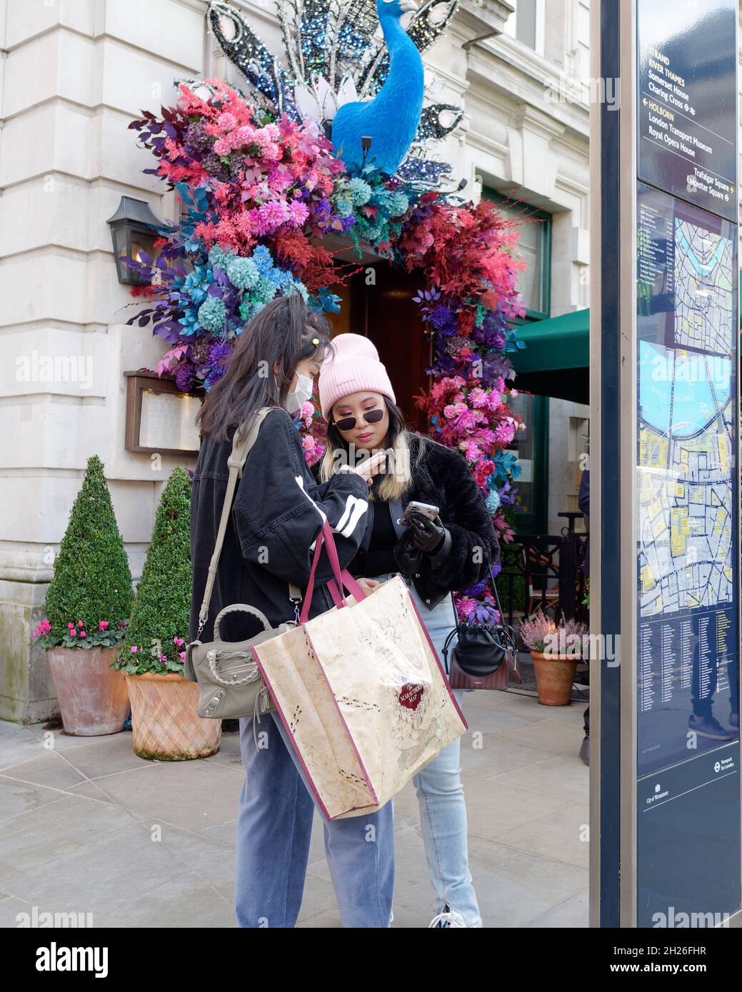 Londra, Greater London, Inghilterra, ottobre 05 2021: Giovani donne alla moda con borse per lo shopping controllare i loro telefoni a Covent Garden. Uno indossa occhiali da sole Foto Stock