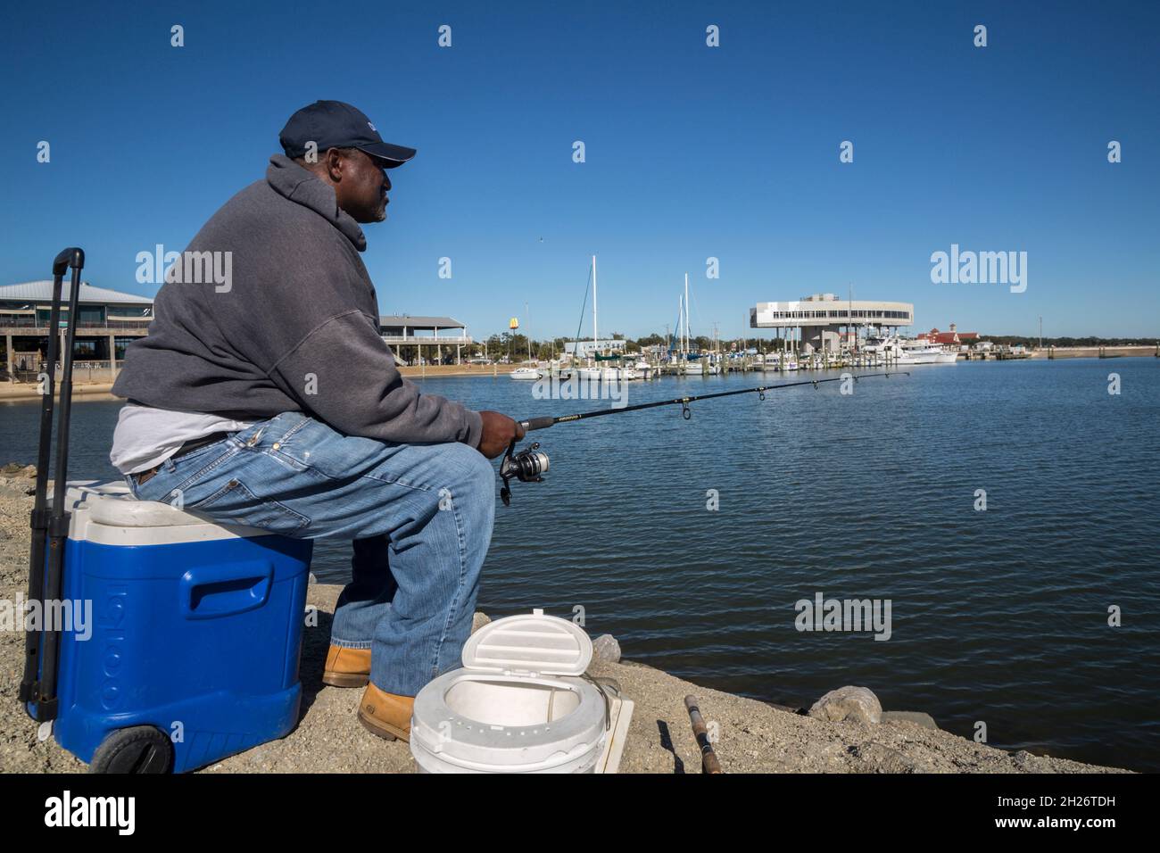 Uomo nero anziano seduto sul refrigeratore e la pesca al porto turistico di Long Beach, Mississippi Foto Stock