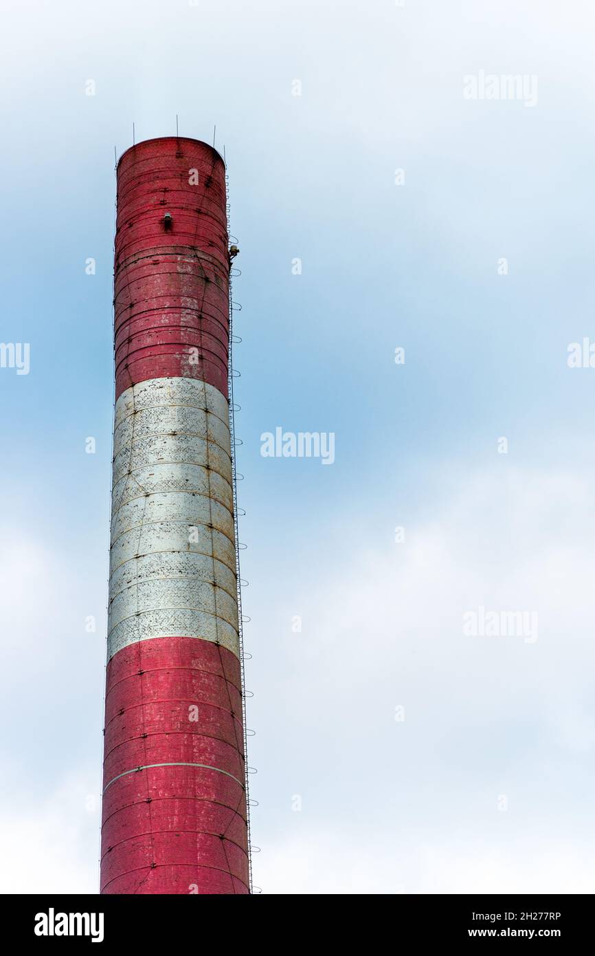 Vecchio camino di fabbrica in mattoni dipinto di bianco e rosso contro il blu, cielo nuvoloso Foto Stock