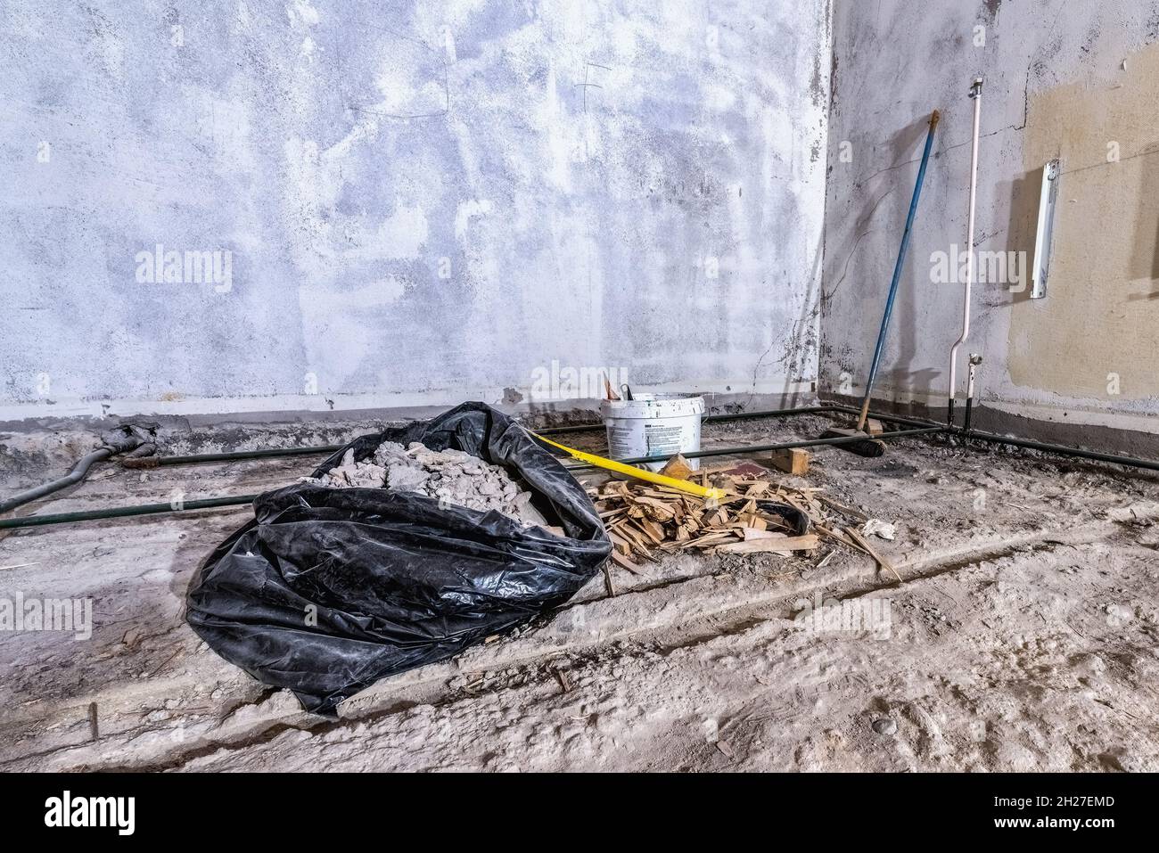 Scarti di costruzione in sacchetto di plastica nero e trucioli di legno su un vecchio pavimento di cemento, da camera demolita, spazzatrice, palanchino. Angolo della camera, ampia vista Foto Stock