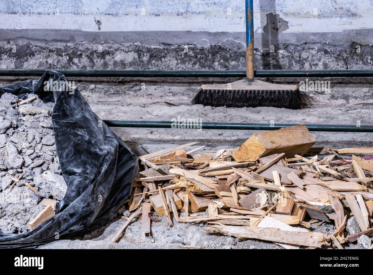Rifiuti di costruzione detriti in busta di plastica nera e su vecchio pavimento di cemento, da sala demolita, spazzatura sfocata sullo sfondo, vista ravvicinata Foto Stock
