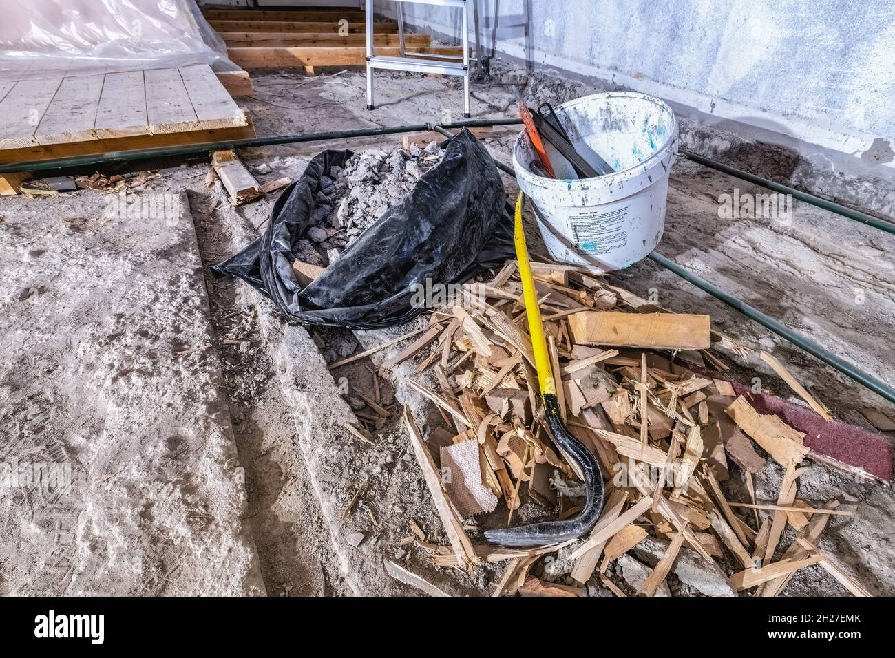 Rifiuti di costruzione detriti in sacchetto di plastica nera trucioli di legno su vecchio pavimento in cemento, in parte abbattuto vecchio pavimento in legno in sala demolita, scopa, crowbar Foto Stock