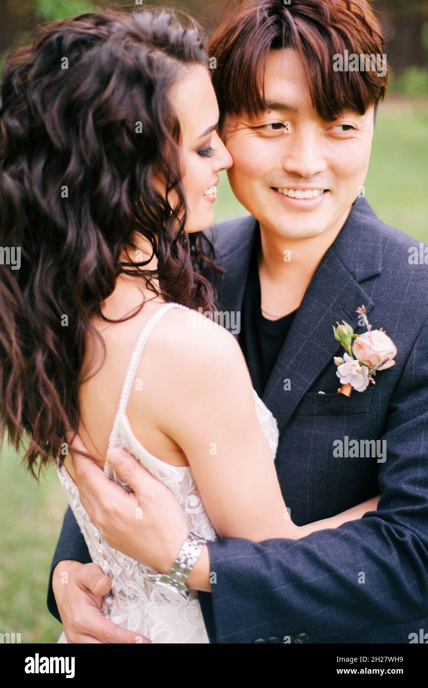 Giorno del matrimonio. Giovani sposi novelli felici nella foresta verde fresca. Coppia internazionale. Ritratto di sposa e sposo. Matrimonio di primavera. Cerimonia nuziale all'aperto. Foto Stock