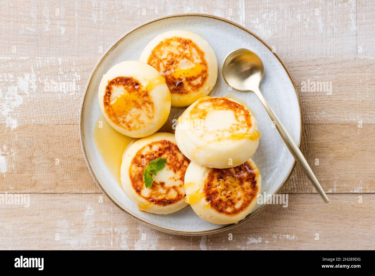 Syrniki, frittelle di formaggio cottage con miele su piatto, isolato su tavola di legno vista dall'alto Foto Stock