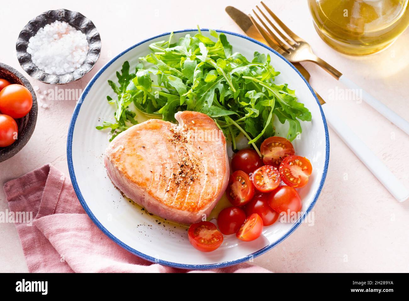 Bistecca di tonno fritta con rucola e pomodori ciliegini, pasto gourmet su un piatto rosa Foto Stock