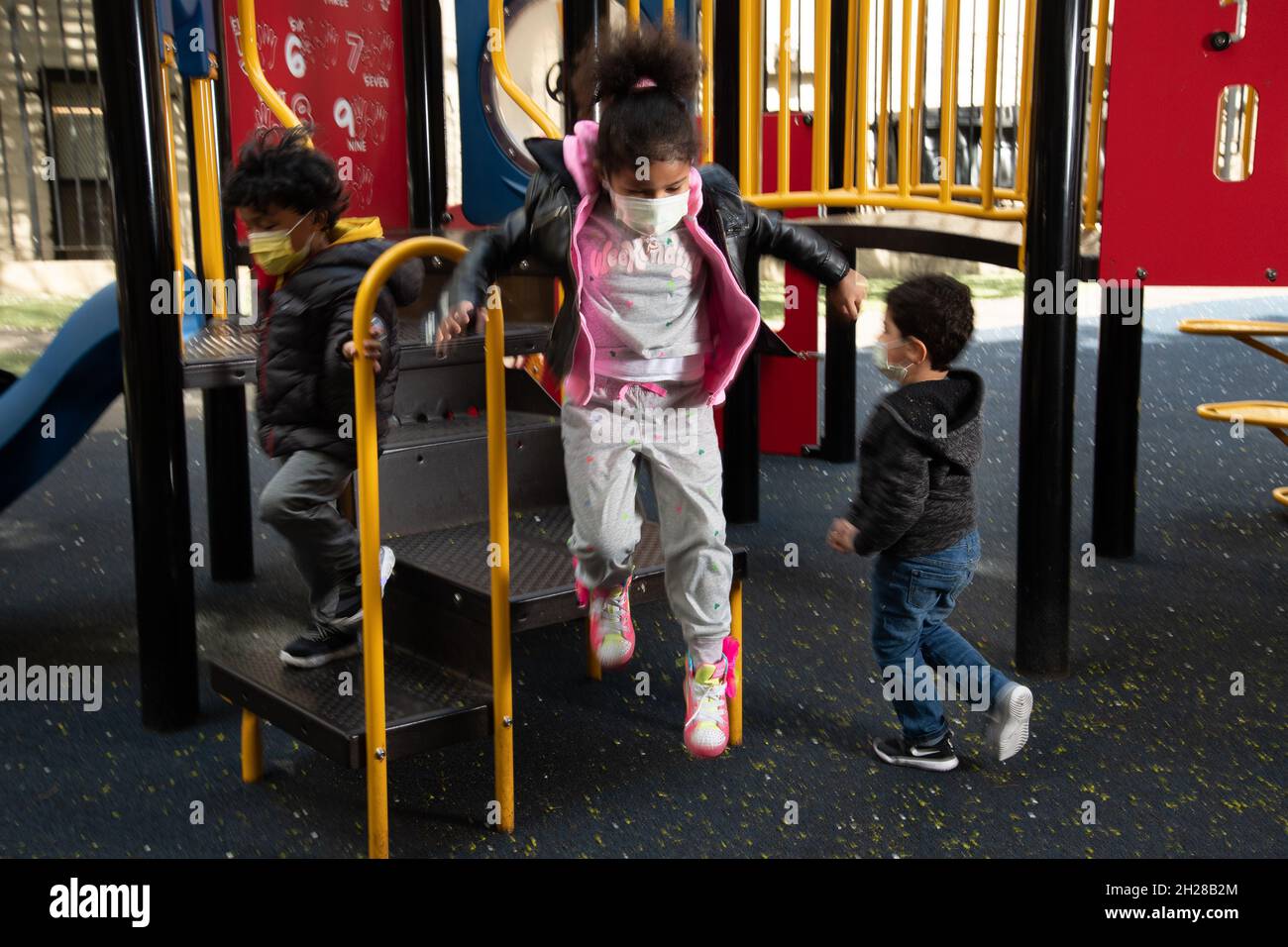 Istruzione Preschool 4-5 anni bambina parco giochi saltare fuori attrezzature parco giochi, indossare maschera per proteggere contro l'infezione Covid-19 Foto Stock