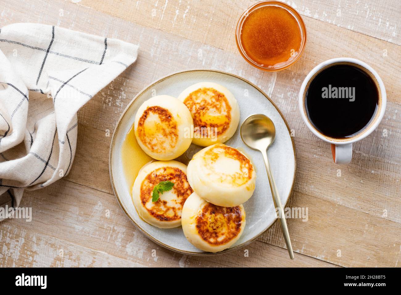 Frittelle di formaggio casolare, frittelle o sciroppi su un tavolo di legno servito con miele e una tazza di caffè nero, vista dall'alto. Ucraino, cibo russo Foto Stock