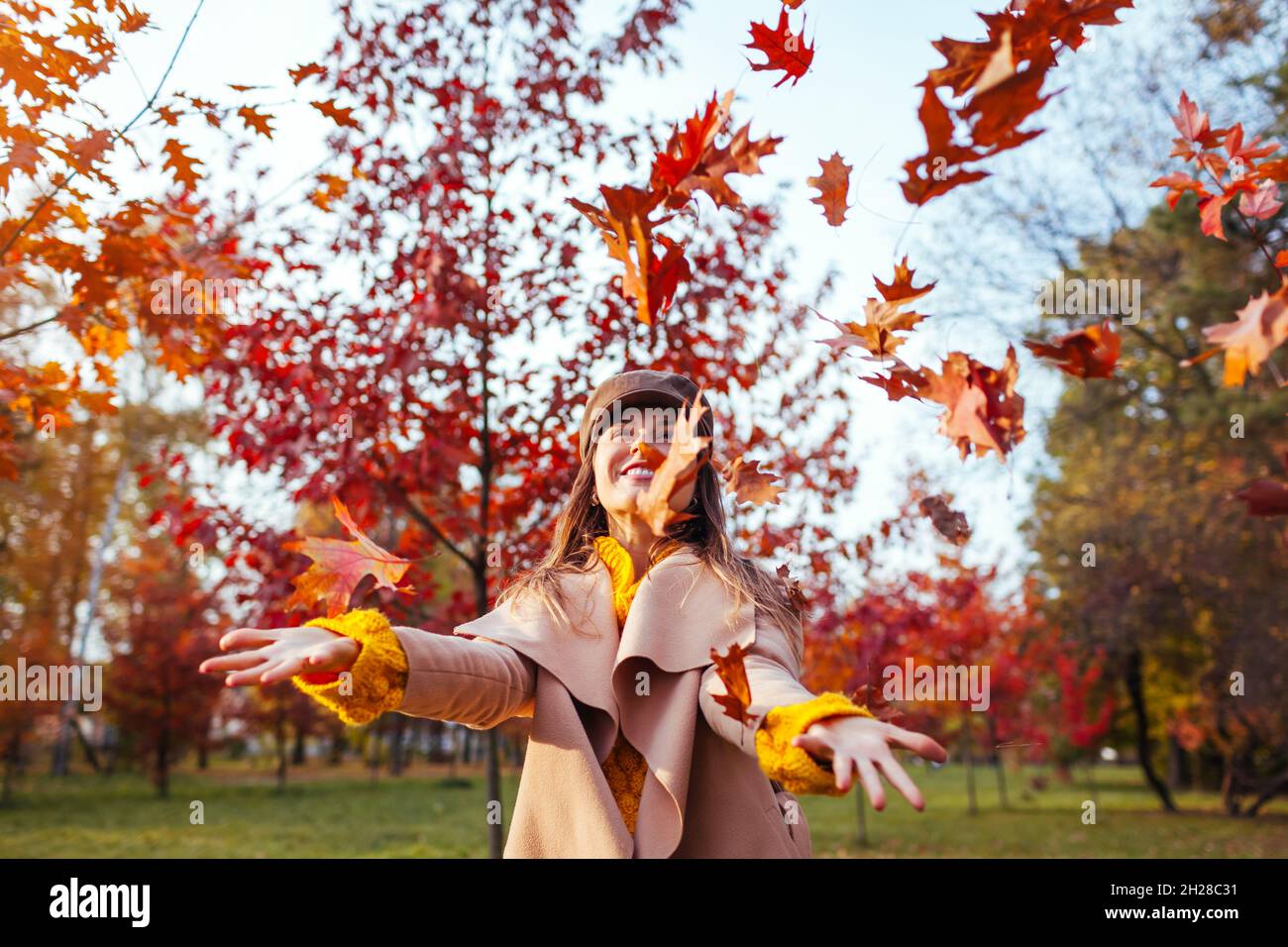 Attività della stagione autunnale. Donna lancio foglie in autunno parco. Giovane donna che si diverte tra gli alberi rossi all'aperto Foto Stock