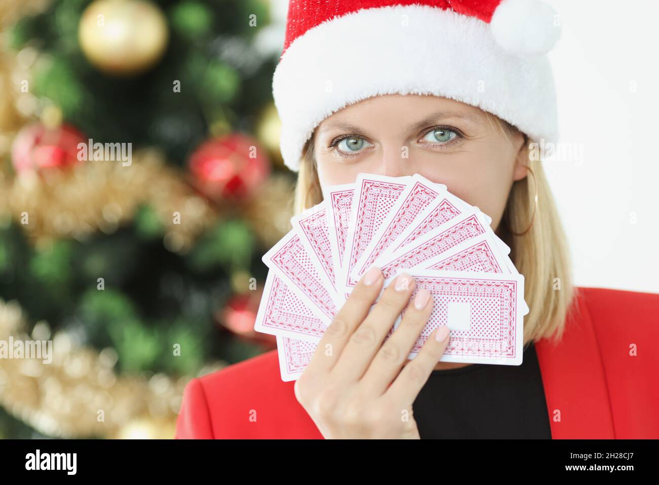 Ritratto di giovane bella donna in babbo natale cappello tenendo carte da gioco sullo sfondo di albero di Capodanno Foto Stock