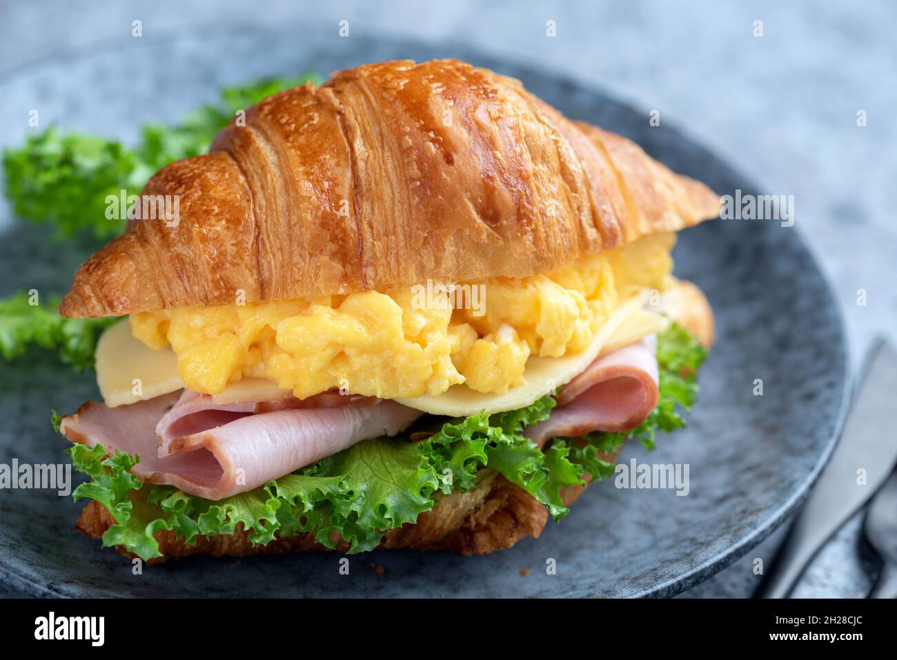 Panino con croissant con uova e prosciutto su un piatto, vista a primo piano. Gustoso sandwich Foto Stock