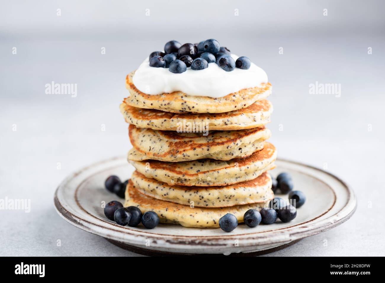 Frittelle di semi di papavero con yogurt e mirtilli su un piatto, frittelle dolci per la colazione, sfondo grigio in cemento Foto Stock