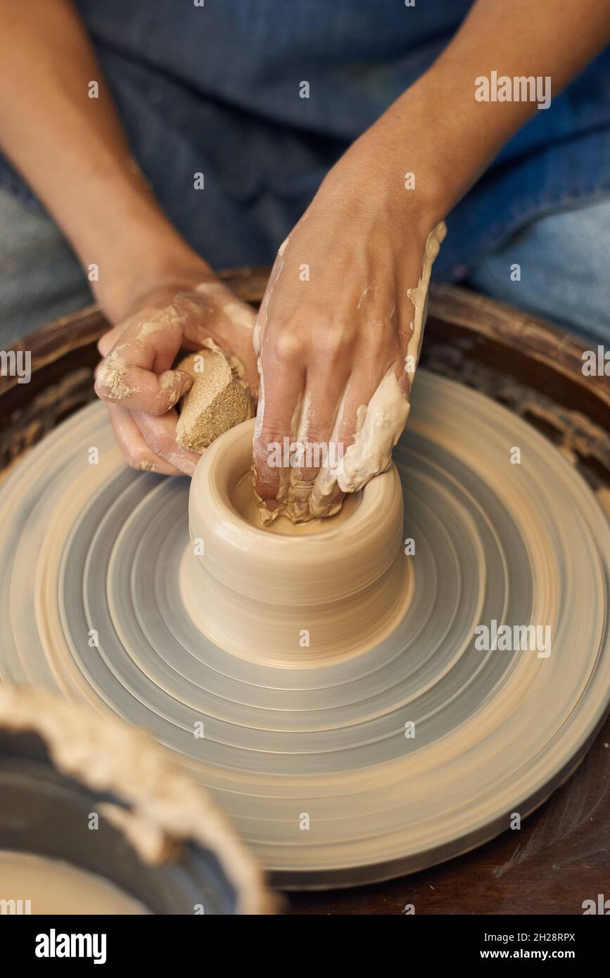 Primo piano di ceramista non riconoscibile che lavora con argilla su ruota di ceramica e rimuovere macchie d'acqua dal vaso con spugna Foto Stock