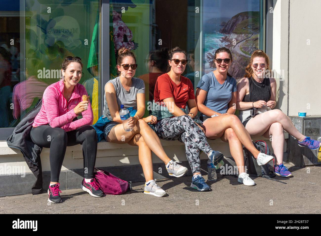 Le giovani donne che siedono fuori negozio, Strand Street, Dingle Peninsula (Corca Dhuibhne), County Kerry, Repubblica d'Irlanda Foto Stock