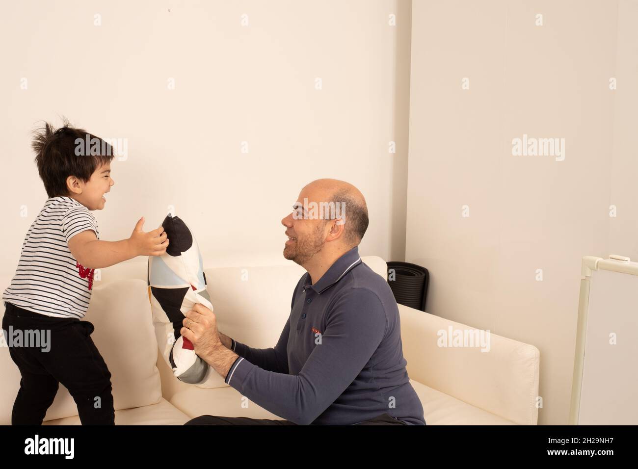 Bambino ragazzo di due anni che gioca a peek un boo con padre e cuscino Foto Stock