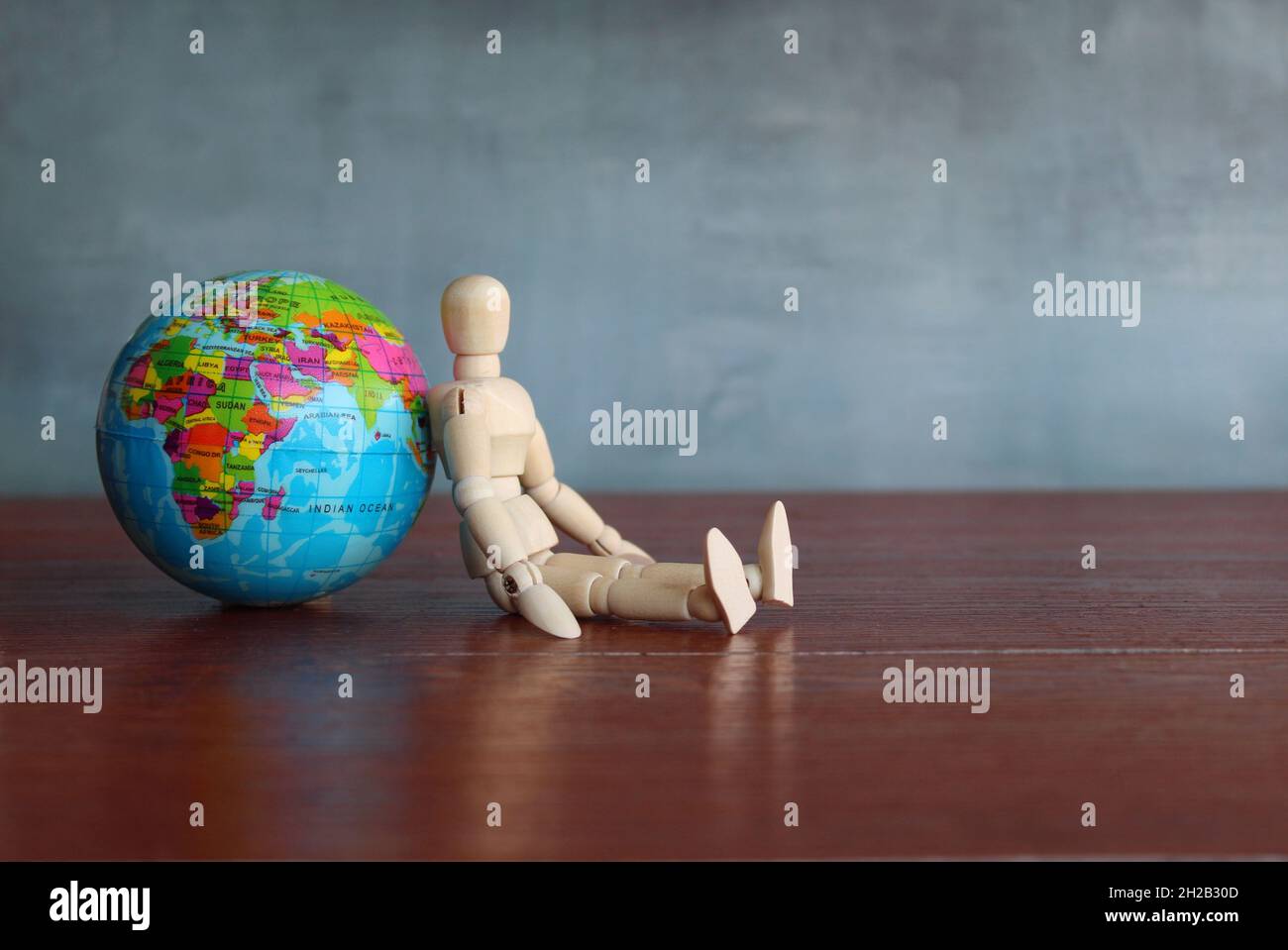 Figura umana in legno appoggiata al globo terrestre. Perso, stanco e rinunciare al concetto Foto Stock