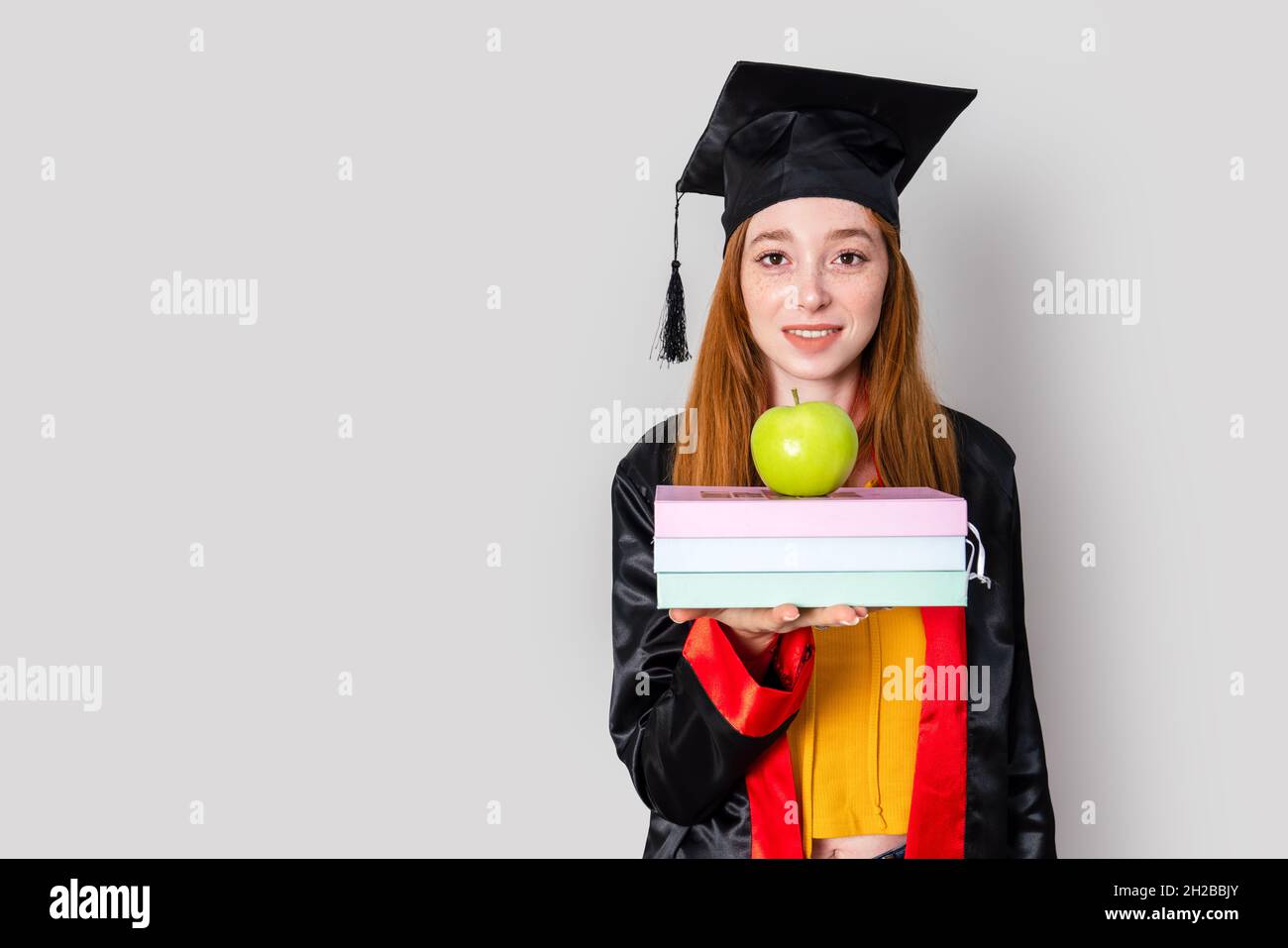 Una studentessa donna dai capelli rossi graziosa, tenendo i suoi libri di studio e celebrando la sua laurea con successo. Foto di alta qualità Foto Stock