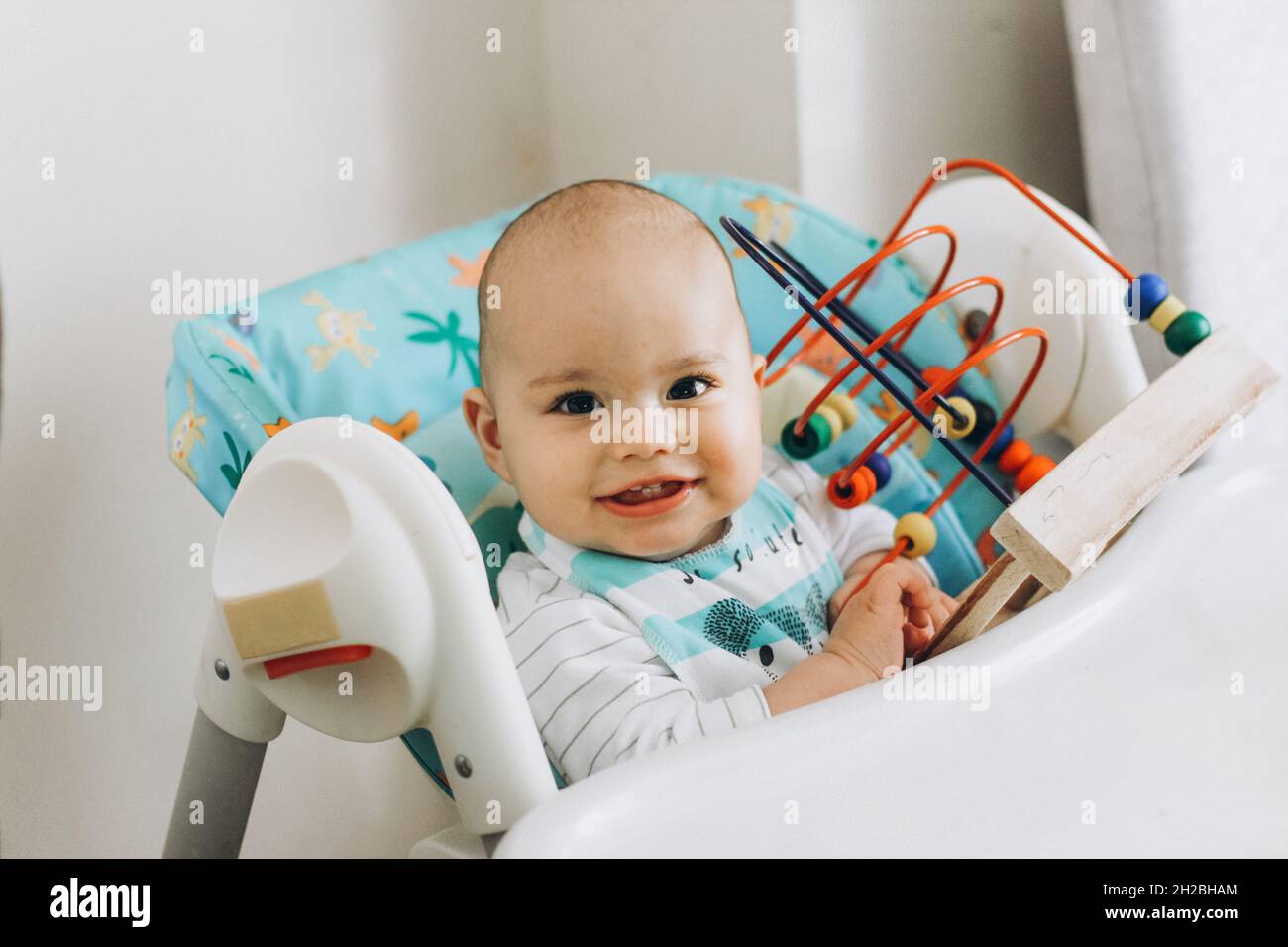 Bambino sorridente felice che gioca i giocattoli in un seggiolone in casa Foto Stock