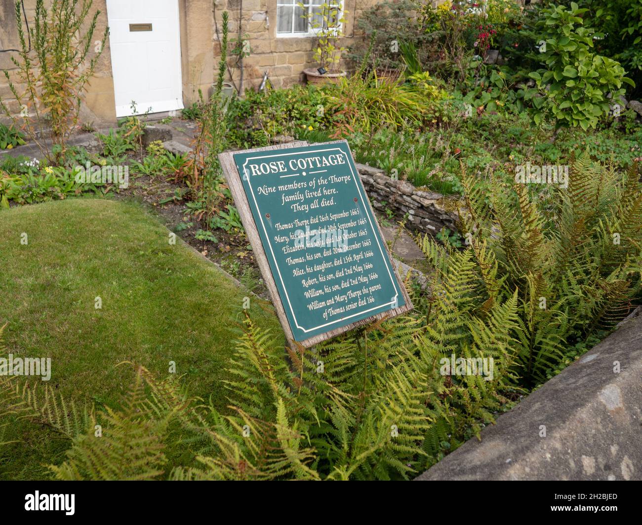 Scheda di informazioni nella parte anteriore di un colorato giardino cottage in estate in uno dei cosiddetti piaga Cottages, Eyam, Derbyshire, Regno Unito Foto Stock