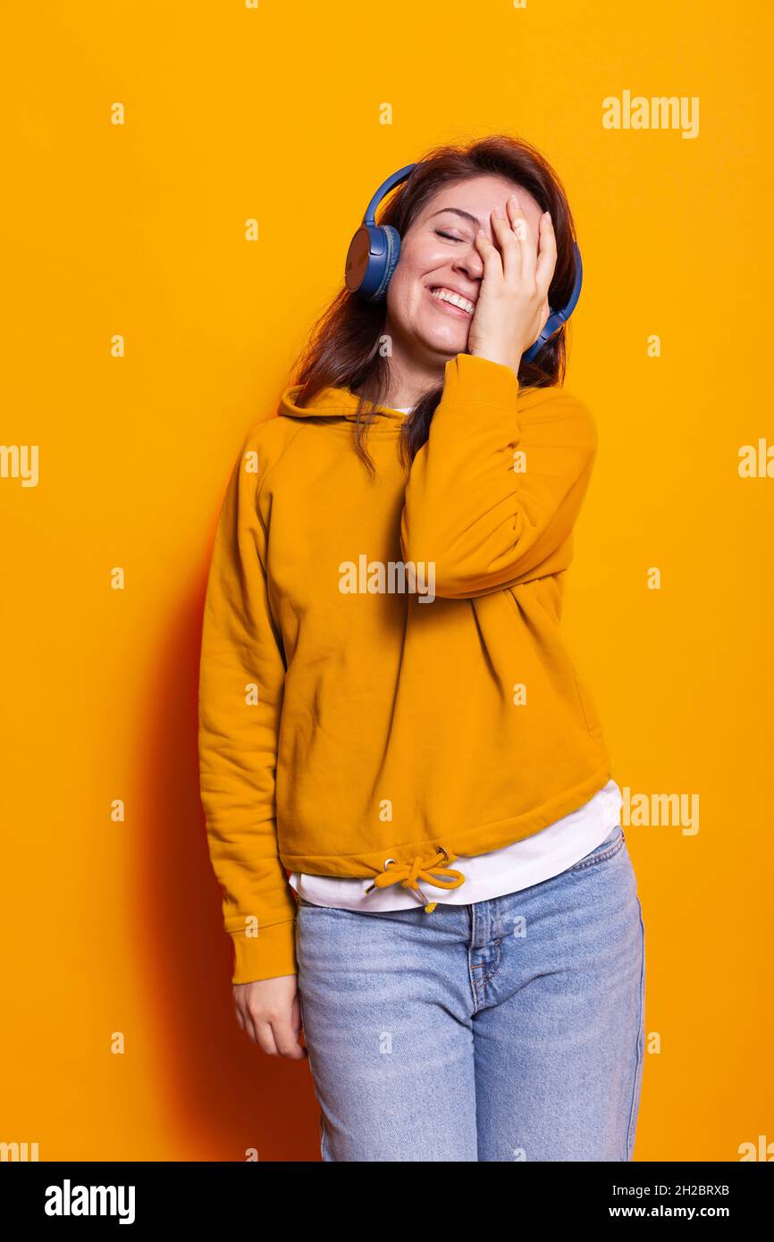 Sorridente persona che copre il viso e ascolta la canzone in cuffia in studio. Donna gioiosa che ama la canzone e i suoni utilizzando la cuffia tenendo la mano sugli occhi chiusi. Adulto che si sente felice Foto Stock