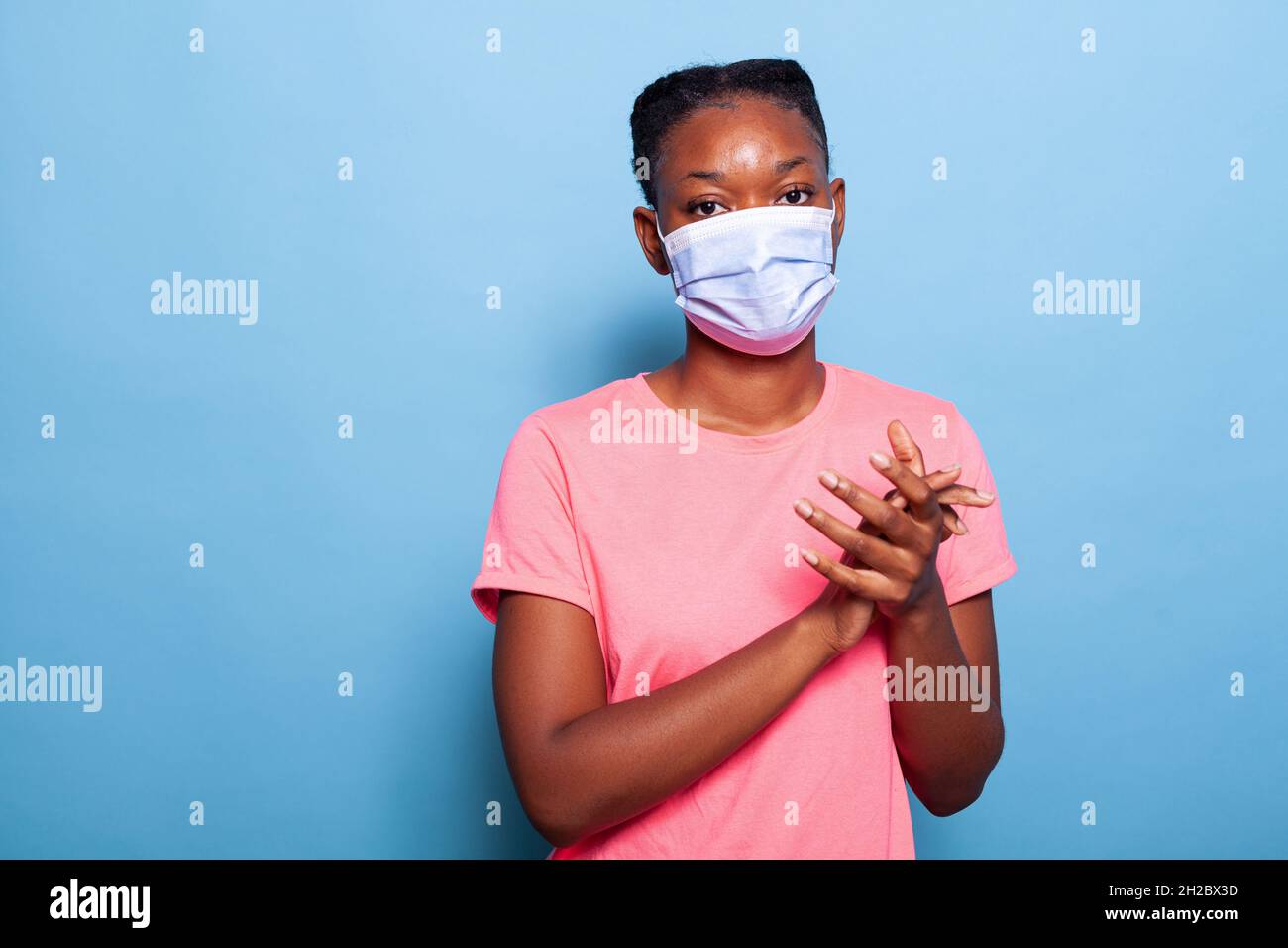 Ritratto africano americano studente con protezione maschera medica viso per prevenire l'infezione con coronavirus clapping e applauding felice e gioioso in studio con sfondo blu. Concetto di vittoria Foto Stock