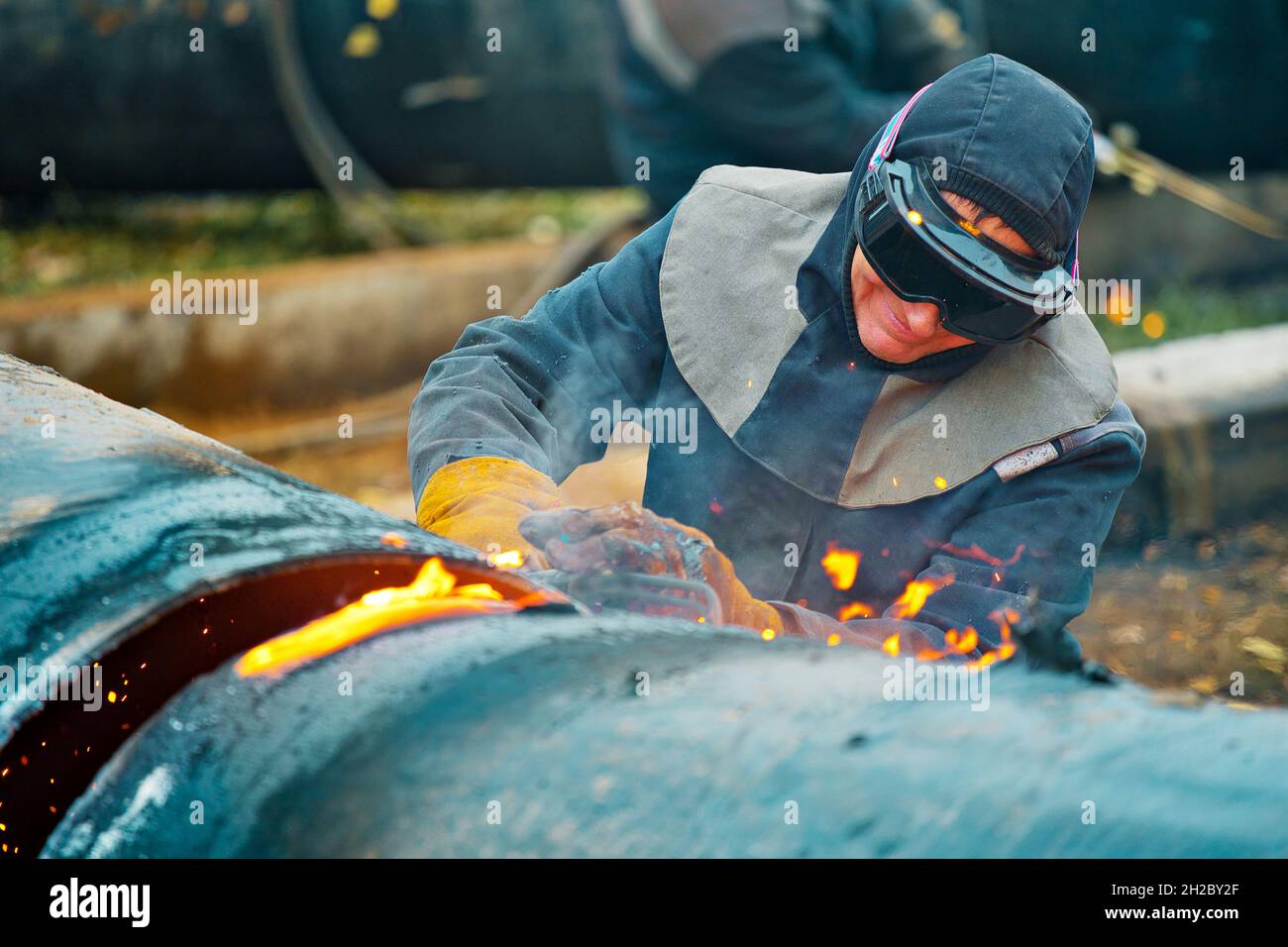 La saldatrice taglia grandi tubi metallici con saldatura in ocetilene. Un lavoratore in strada taglia tubi di grande diametro durante il giorno e scintille e fuoco volare. Foto Stock