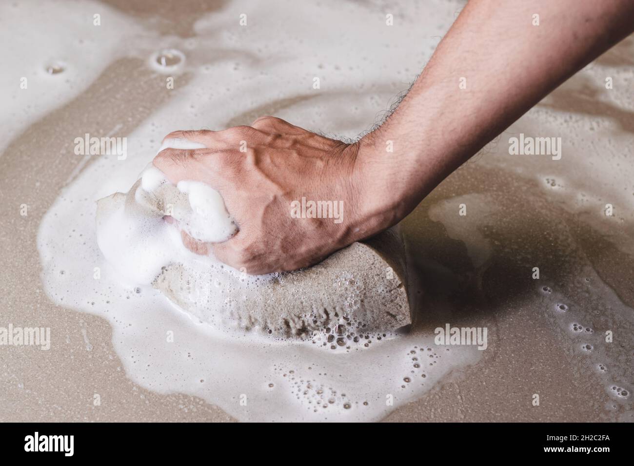 Le mani degli uomini stanno usando una spugna che pulisce il pavimento della piastrella. Foto Stock