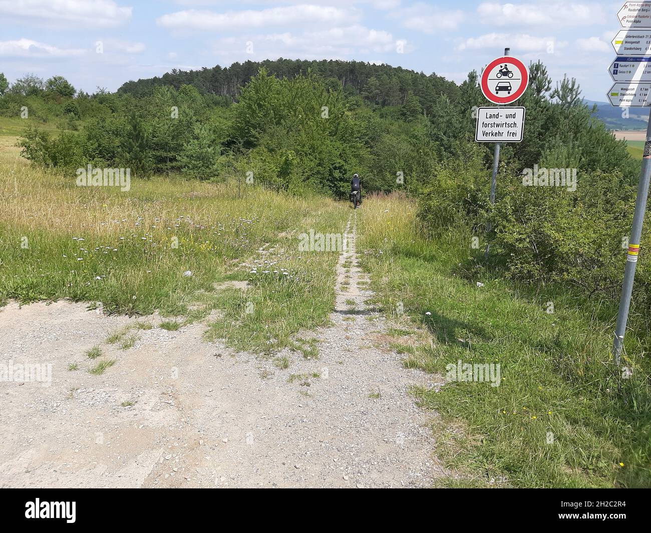 Ciclista su una strada a colonne sull'ex confine tedesco-tedesco dei Monti Rhoen, Germania, Baviera Foto Stock