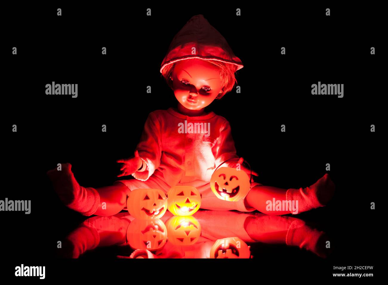 Bambola antica seduta con zucche tra le gambe con illuminazione rossa, Halloween, paura, terrore. Foto Stock