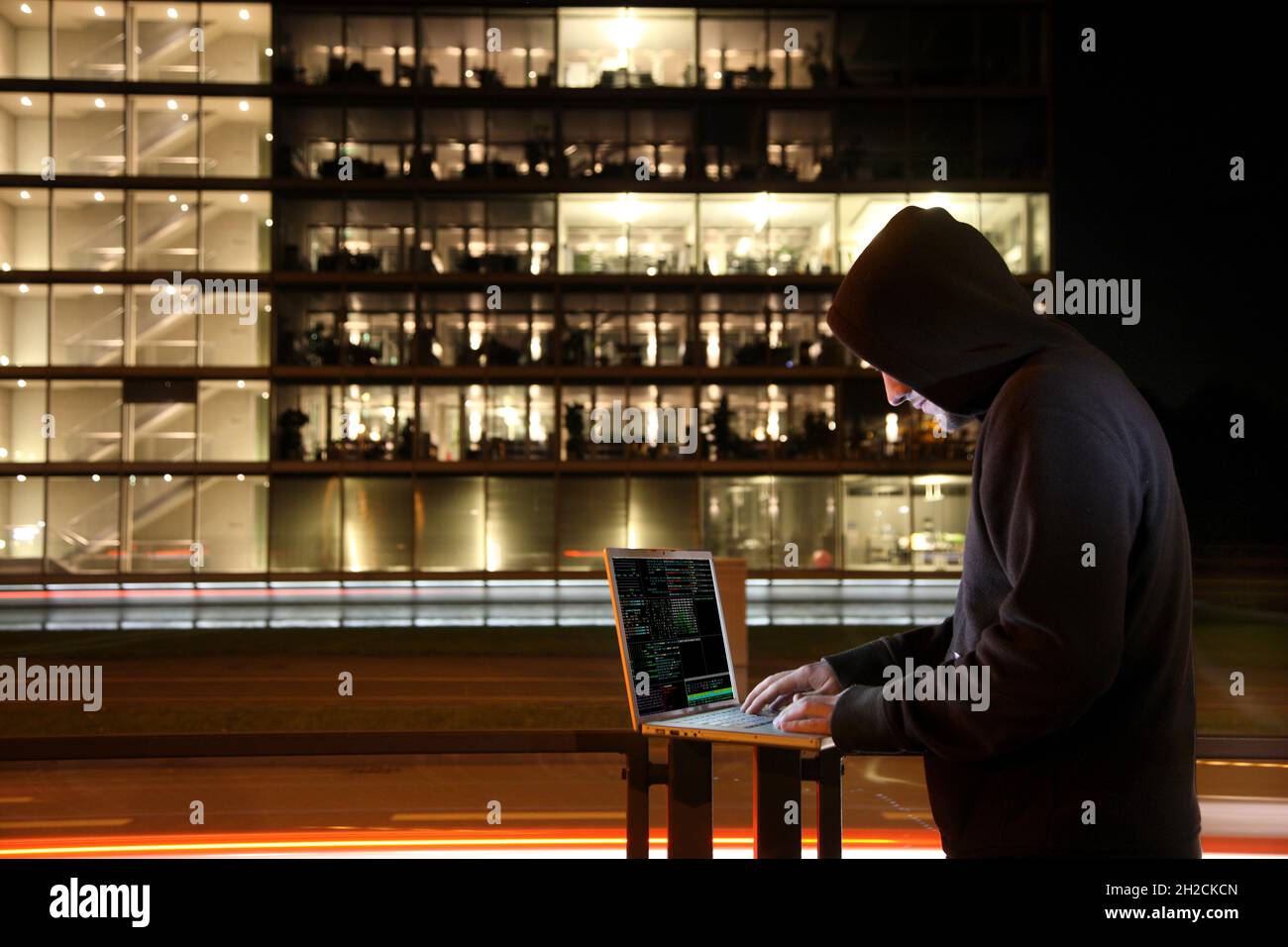 Immagine simbolica computer hacker, computer crimine, cyber crimine, cyber attacco, hacker con notebook di fronte a un edificio di uffici, hacks in computer syst Foto Stock