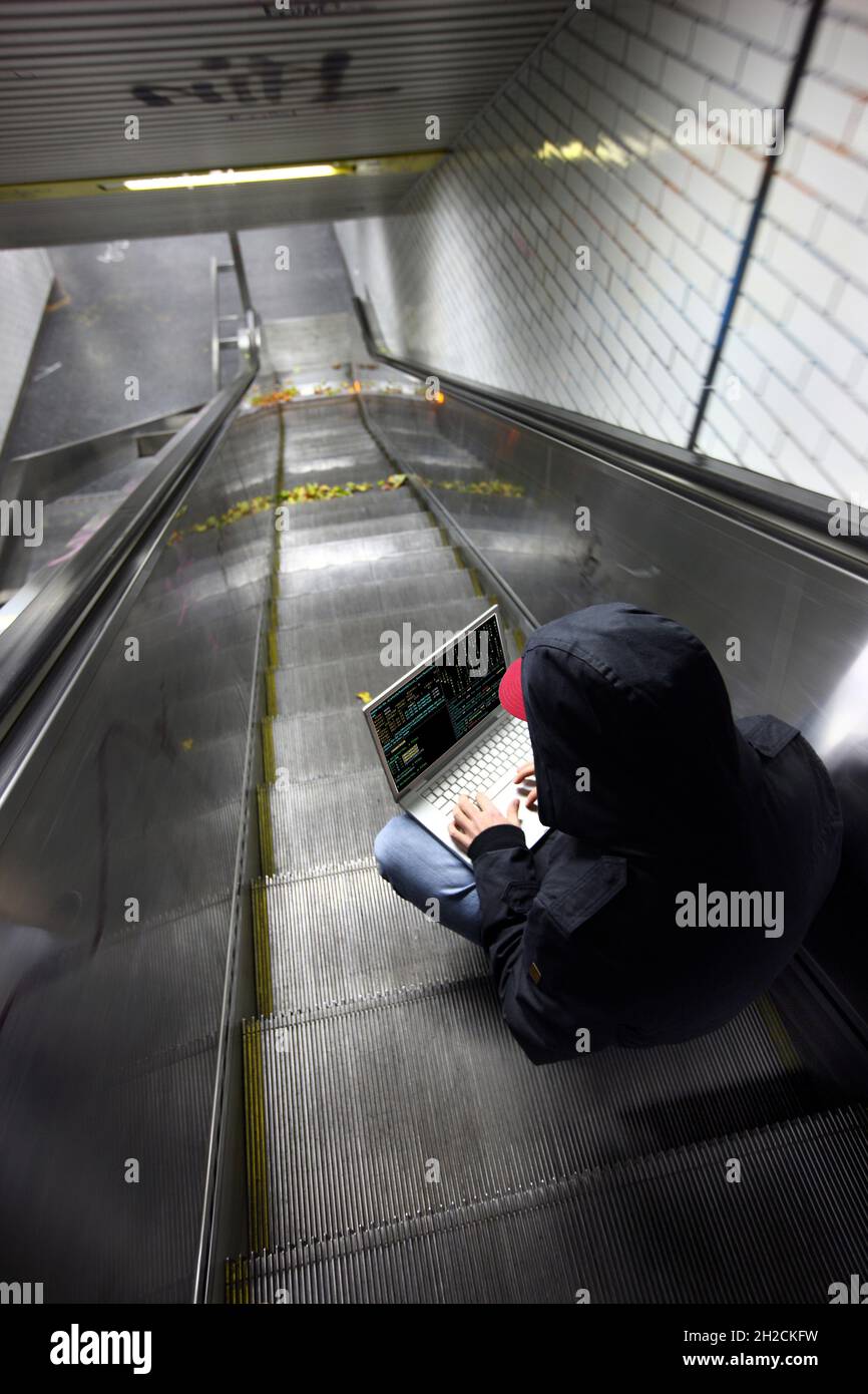 Immagine simbolica computer hacker, computer crime, cyber crime, cyber attack, hacker con computer portatile in una stazione della metropolitana, Foto Stock